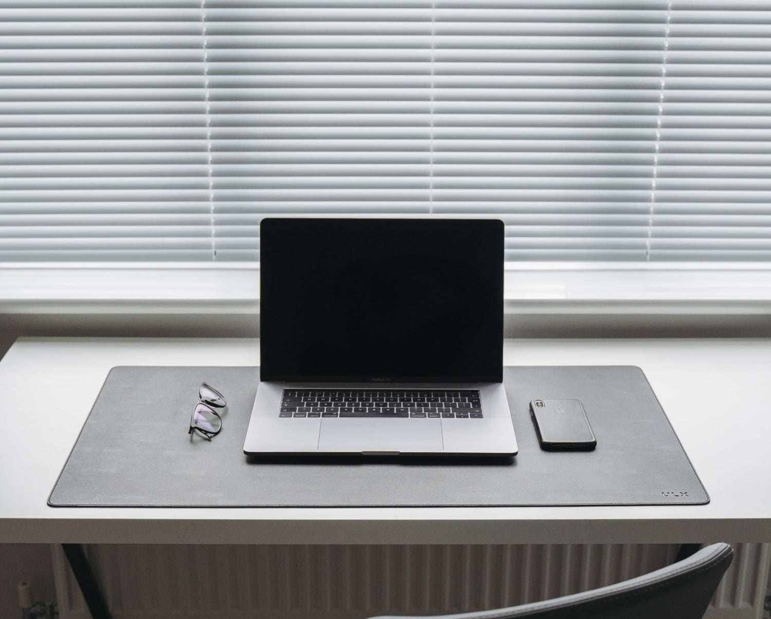 ULX desk mat on a desk with laptop, glasses and phone